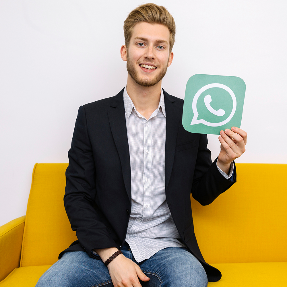 homem-loiro-sentado-em-sofá-amarelo-segurando-placa-do-whatsapp-business